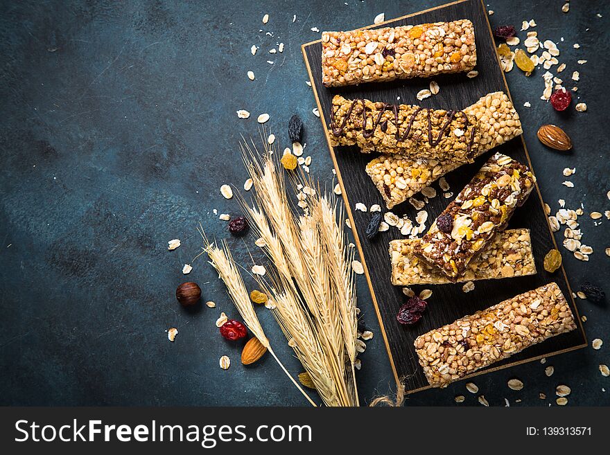 Granola bar. Healthy snack. Cereal granola bar with nuts, fruit and berries on cutting board at dark stone table. Top view copy space. Granola bar. Healthy snack. Cereal granola bar with nuts, fruit and berries on cutting board at dark stone table. Top view copy space.