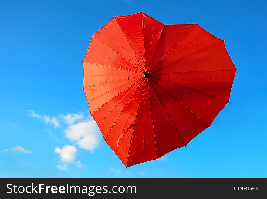 Red, scarlet umbrella in the shape of heart against blue sky on clear, sunny day. Valentine`s day concept