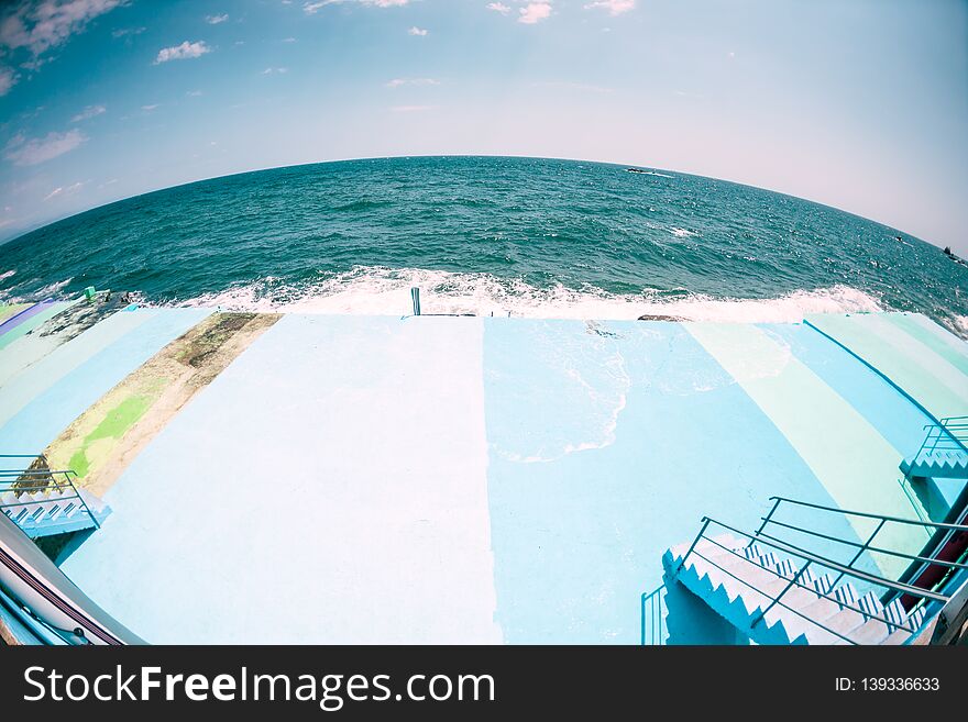 Pier on the waterfront. Sea waves break on the breakwater. Ocean landscape. Quay street resort town. Foam from sea water