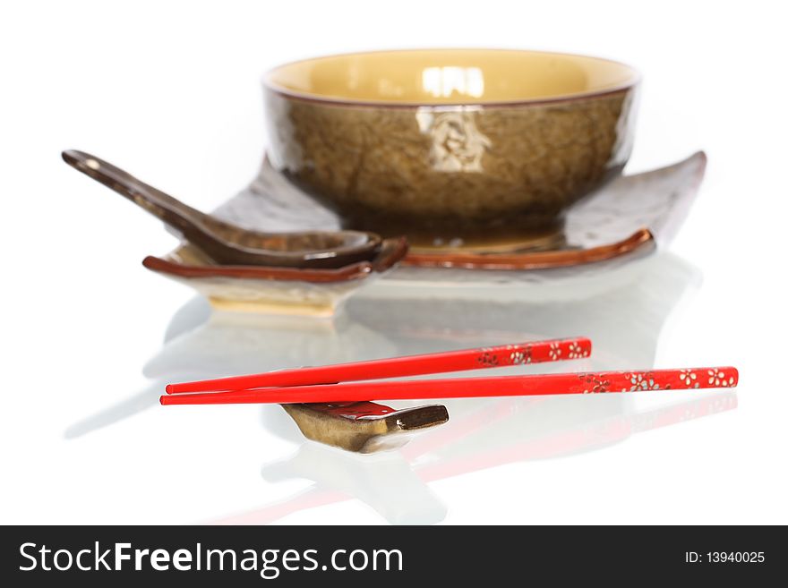 Pair of red chopsticks on white background with set of ceramic japanese dishware