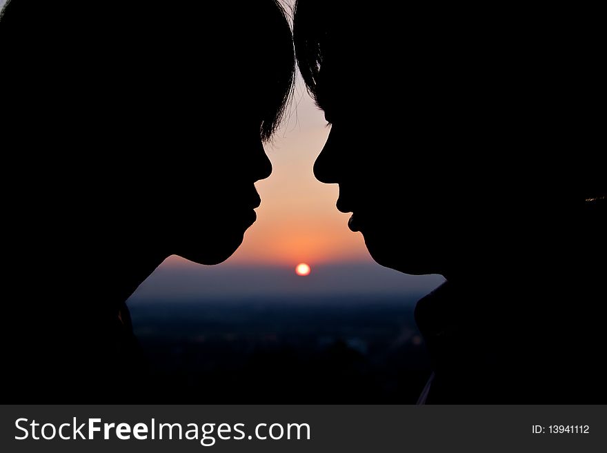 Beautiful silhouettes of man and woman face close together during sunset
