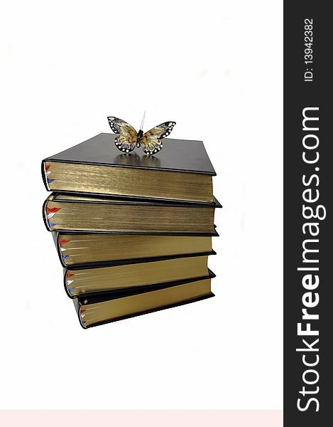 Five books with gilt edges on the upper edge in an uneven stack. On top of the book artificial butterfly. Photography.