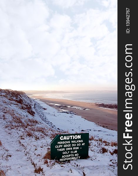 A caution sign on a cliff edge in snow covered ballybunion. A caution sign on a cliff edge in snow covered ballybunion