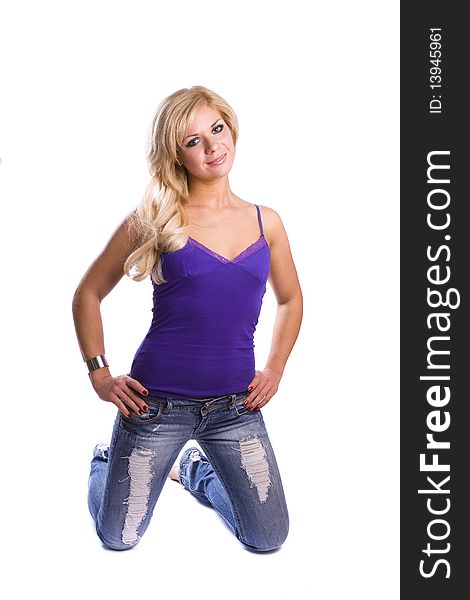 Blond woman in blue jeans and sleeveless violet top is in the kneeling position on floor. Young woman with smoky eyes make-up isolated on white. Blond woman in blue jeans and sleeveless violet top is in the kneeling position on floor. Young woman with smoky eyes make-up isolated on white.