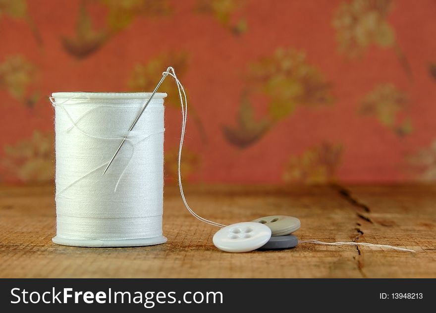 Spool of white thread with a needle and buttons on a rustic table. Spool of white thread with a needle and buttons on a rustic table.