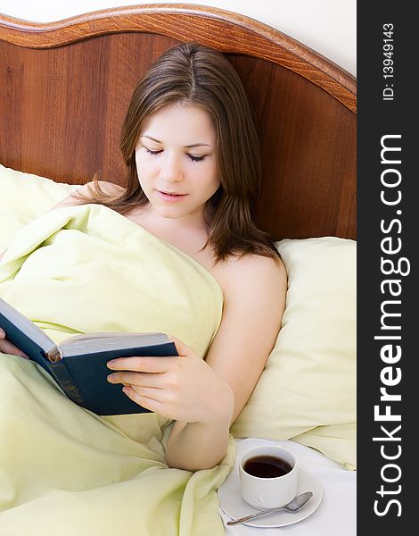 Young beautiful woman with book and cup of coffee in the bed. Young beautiful woman with book and cup of coffee in the bed