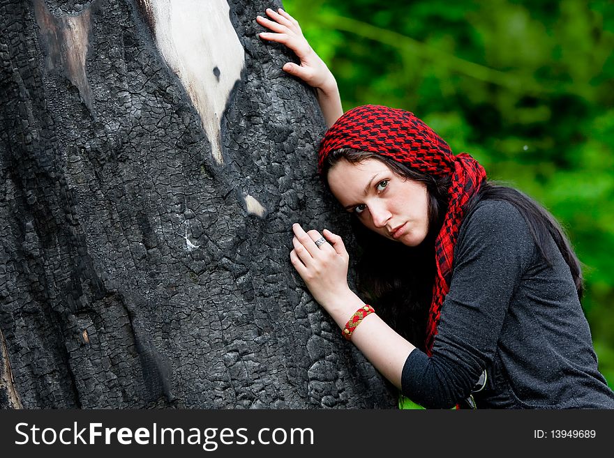 Girl in red scarf leaned against the charred tree