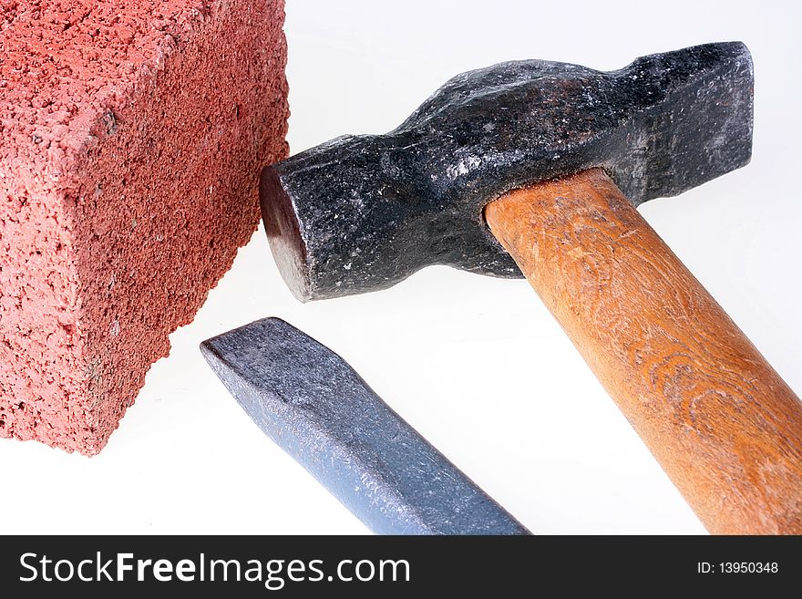 Building materials and tools: a chisel and a hammer with a brick from red clay.