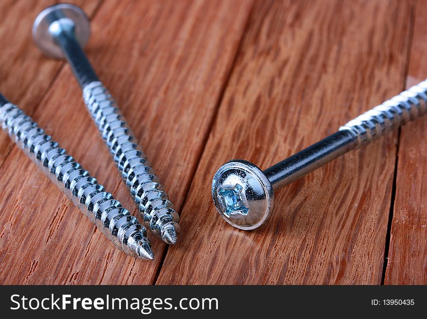 Long metal screws for a crosswise screw-driver on a wooden table.