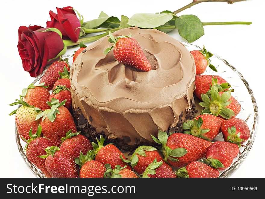 A chocolate cake surrounded by fresh strawberries and red roses on horizontal white background, copy space. A chocolate cake surrounded by fresh strawberries and red roses on horizontal white background, copy space