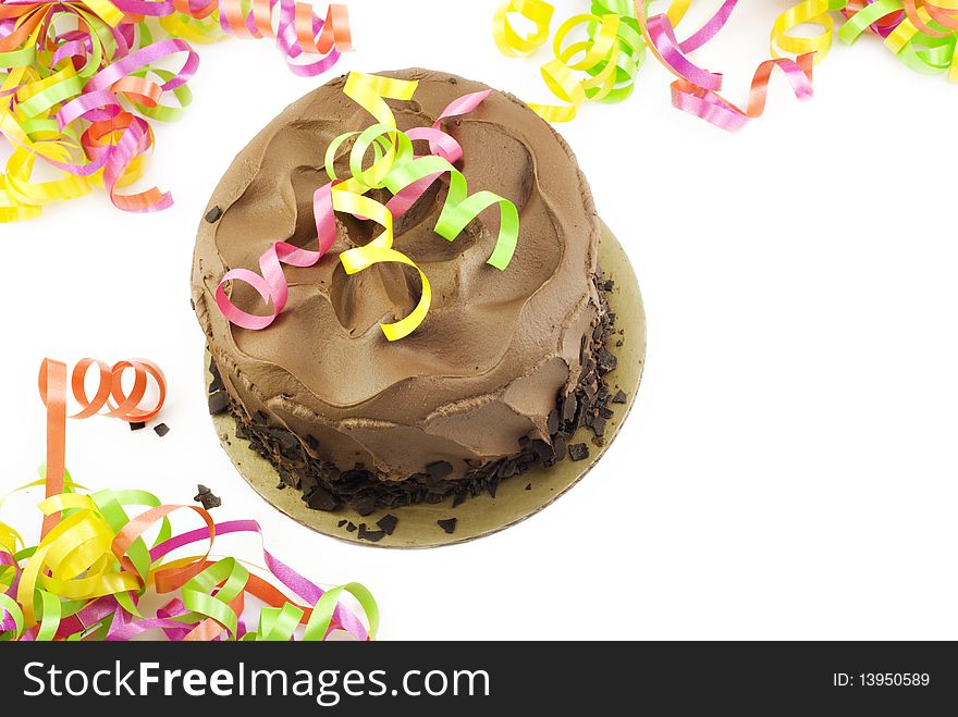 A chocolate fudge layer cake with colorful party ribbons on a white horizontal background with copy space, top view. A chocolate fudge layer cake with colorful party ribbons on a white horizontal background with copy space, top view