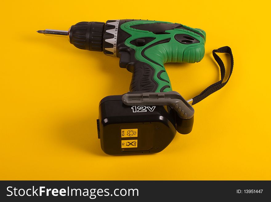 Green cordless screwdriver on a yellow background