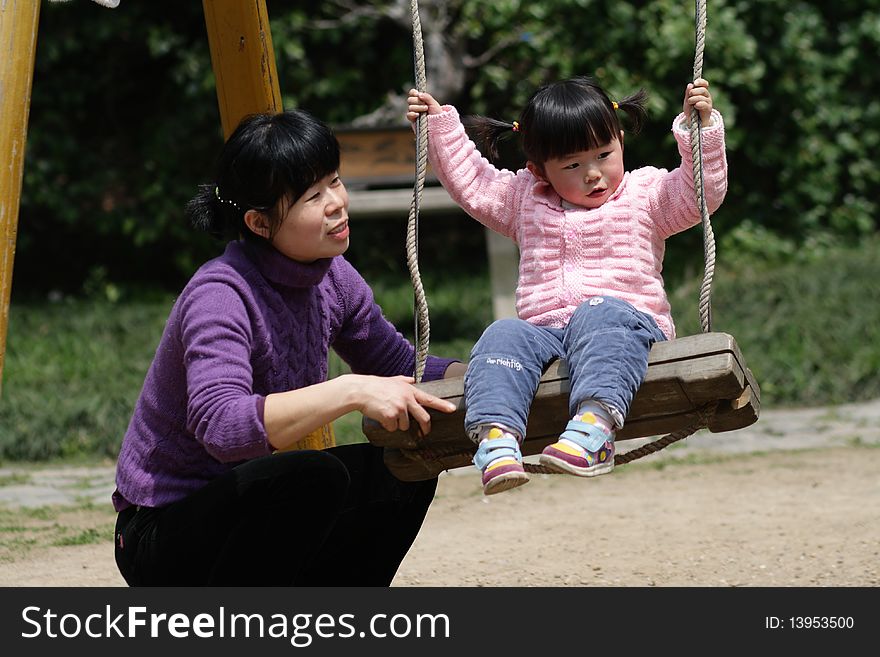He girl is playing on the swingï¼Œher mother looking after her carefully. He girl is playing on the swingï¼Œher mother looking after her carefully