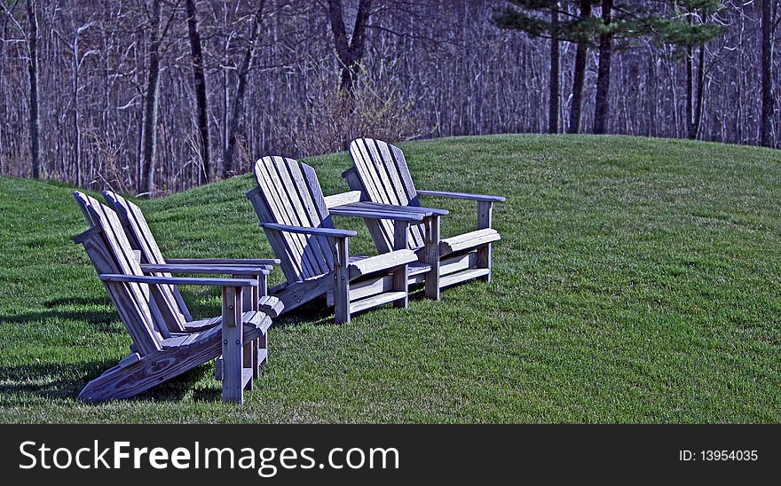 Group of four wooden adirondack chairs sunlit on a grass knoll. Group of four wooden adirondack chairs sunlit on a grass knoll