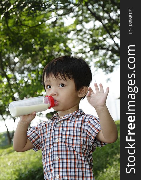 An Asian boy drinking from a milk bottle at a public park waving at the camera. An Asian boy drinking from a milk bottle at a public park waving at the camera