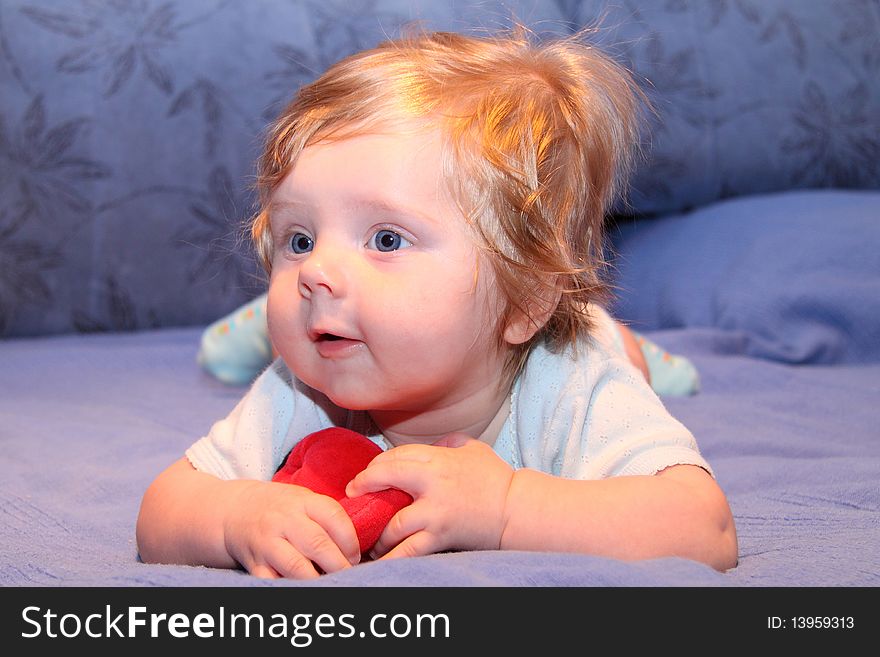 Nice blue-eyed baby playing with red toy on blue sofa. Nice blue-eyed baby playing with red toy on blue sofa