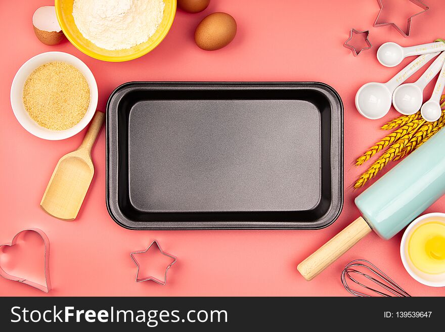 Baking ingredients and empty baking tray on pink background, flat lay. Ingredients, kitchen items for baking. Kitchen utensils, flour, eggs, sugar. Text space, top view