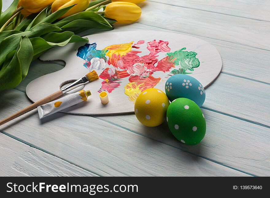 Easter Background With Colorful Eggs, Paints, Brushes And Yellow Tulips On Wooden Table. Top View With Copy Space