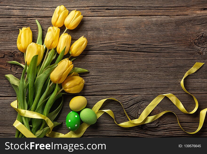 Yellow tulips in a paper bag, a nest with Easter eggs on a wooden background. Top view with copy space