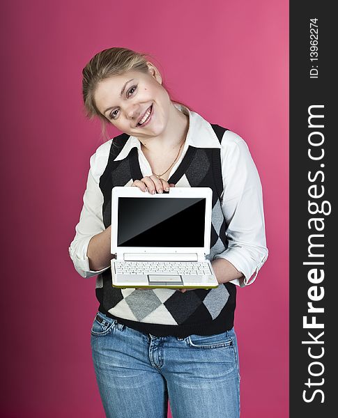 Blond young woman with laptop posing on pink background, studio shot