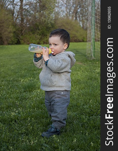 A toddler standing on a grassy field drinking from a plastic bottle. A toddler standing on a grassy field drinking from a plastic bottle.