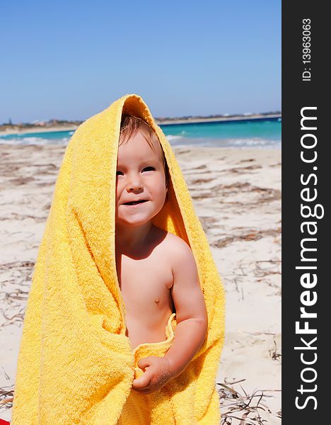 Charming little girl in a yellow towel on the beach as a symbol of childhood happiness and joy