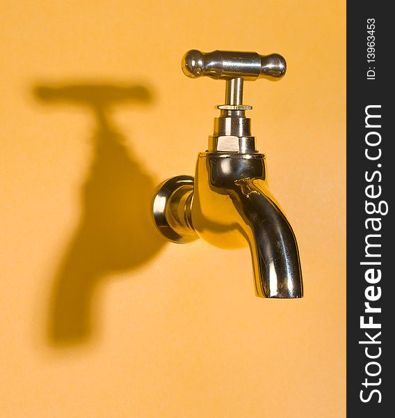 Close-up gold faucet in orange wall