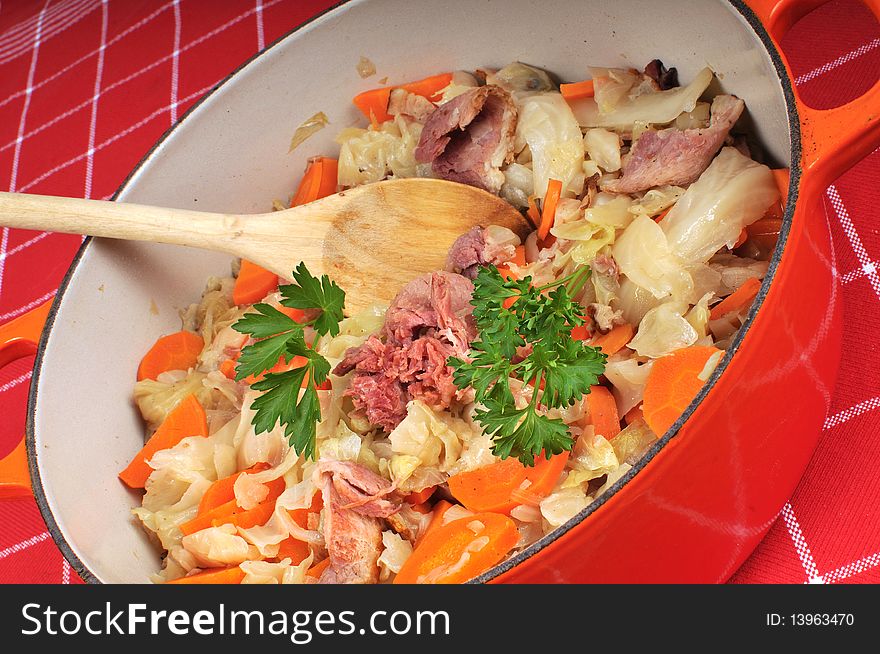 Large pot filled with ham, cabbage and carrots and parsley. The table is dressed with a checkered red cloth. Large pot filled with ham, cabbage and carrots and parsley. The table is dressed with a checkered red cloth.