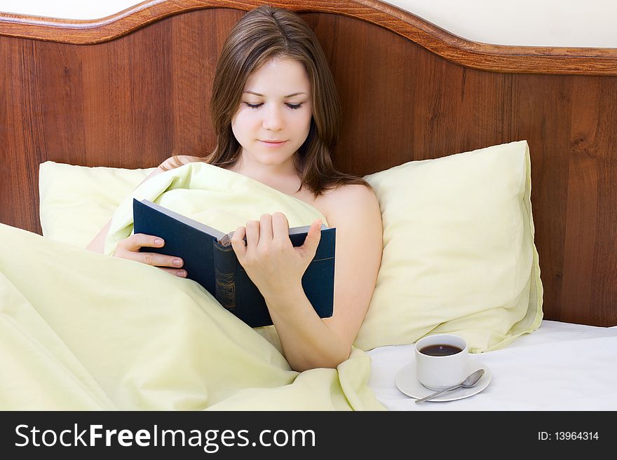 Young beautiful woman with book and cup of coffee in the bed. Young beautiful woman with book and cup of coffee in the bed