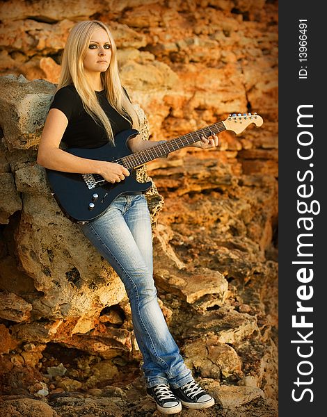 Series. The beautiful blonde with a guitar on rock background