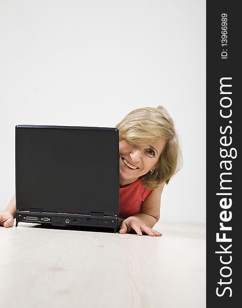 Senior woman laughing and looking behind a laptop while lying down on wooden floor,see more in People on couch or wooden floor. Senior woman laughing and looking behind a laptop while lying down on wooden floor,see more in People on couch or wooden floor