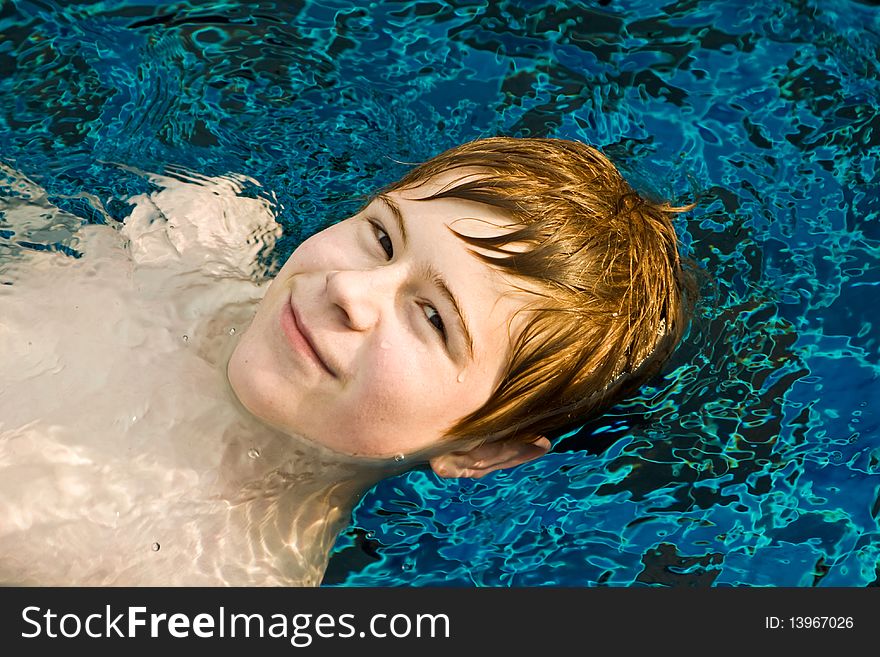 Boy is sminning in a pool and enjoying the water, he looks relaxed. Boy is sminning in a pool and enjoying the water, he looks relaxed