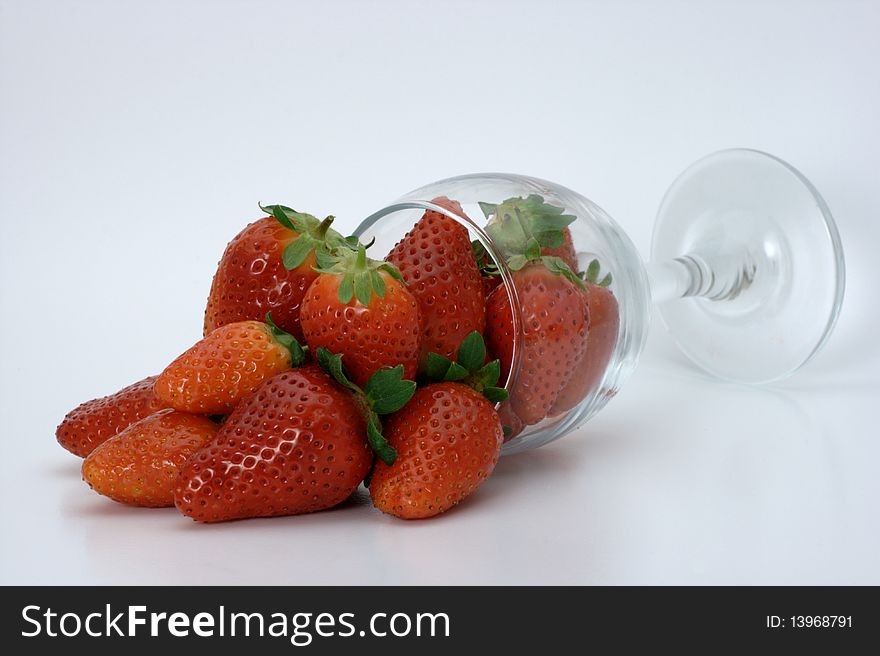 Ripe red strawberries spilling out of an over turned wine glass on a white background. Ripe red strawberries spilling out of an over turned wine glass on a white background.