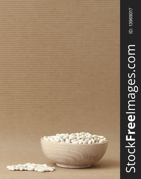 Wooden bowl full of white haricot beans on a brown background