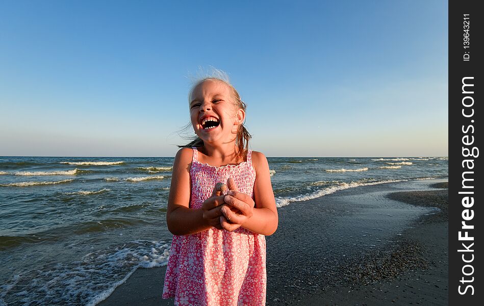 Little pretty girl on summer beach. Cheerful little girl laughs on the background of blue sky and summer sea. Happy child girl playing at beach and having fun