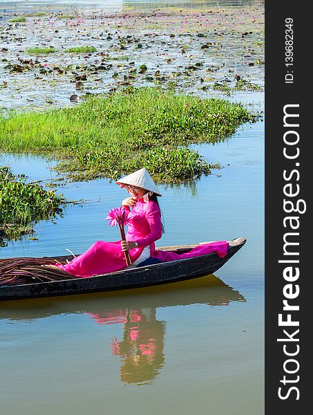 Asian woman in traditional dress Ao Dai sitting on the wooden boat in waterlily pond. Asian woman in traditional dress Ao Dai sitting on the wooden boat in waterlily pond