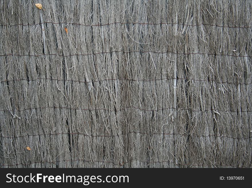 A grey brown brushwood fence showing thin bundles of brushwood woven together by strands of wire