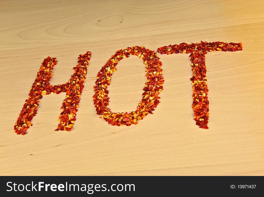 Hot chili flakes, spelled out into the word 'HOT' on a wooden table top.