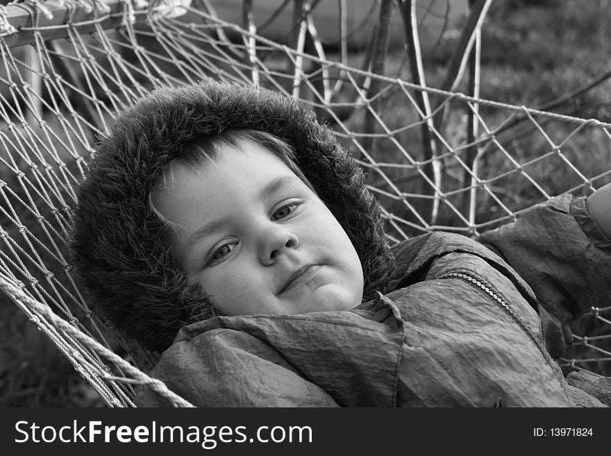 Monochrome portrait of little boy in hammock. He lays quiet and serious looks in the camera. Monochrome portrait of little boy in hammock. He lays quiet and serious looks in the camera