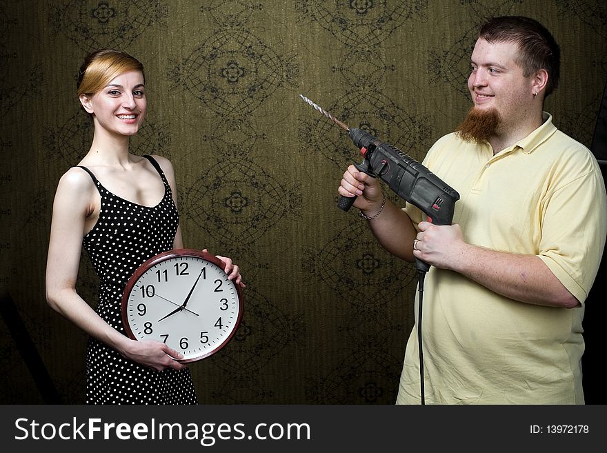 An image of a woman with new clock and a man with drill. An image of a woman with new clock and a man with drill