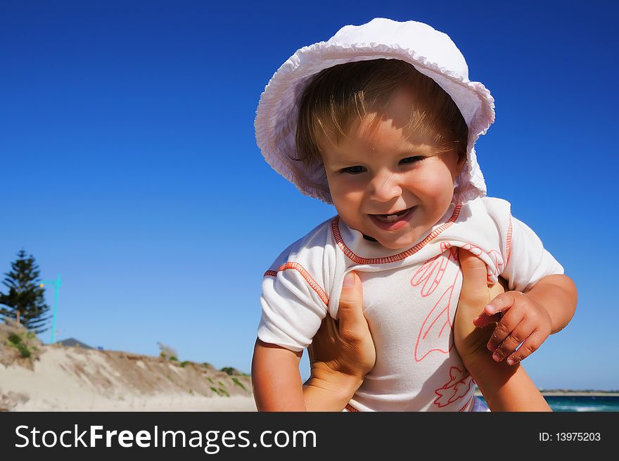 Charming little happy girl laughing in the arms of his mother, against the blue sky