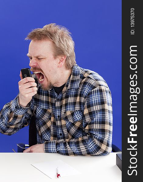 Man shouts on a phone at his office desk.