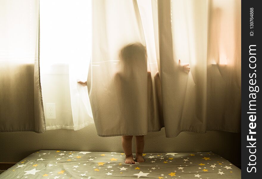 Toddler portrait of a young caucasian boy playing in the window curtains. Toddler portrait of a young caucasian boy playing in the window curtains.