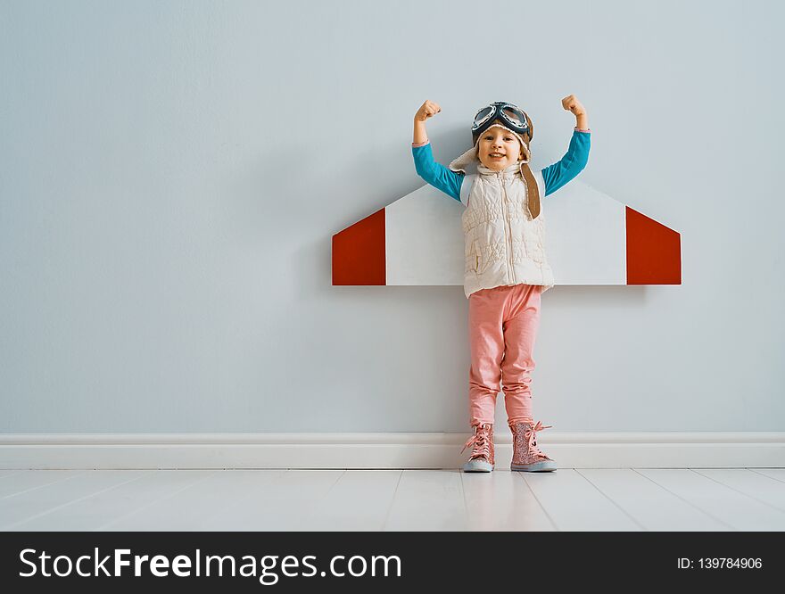 Little child girl in an astronaut costume is playing and dreaming of becoming a spaceman. Portrait of funny kid on a background of grey wall