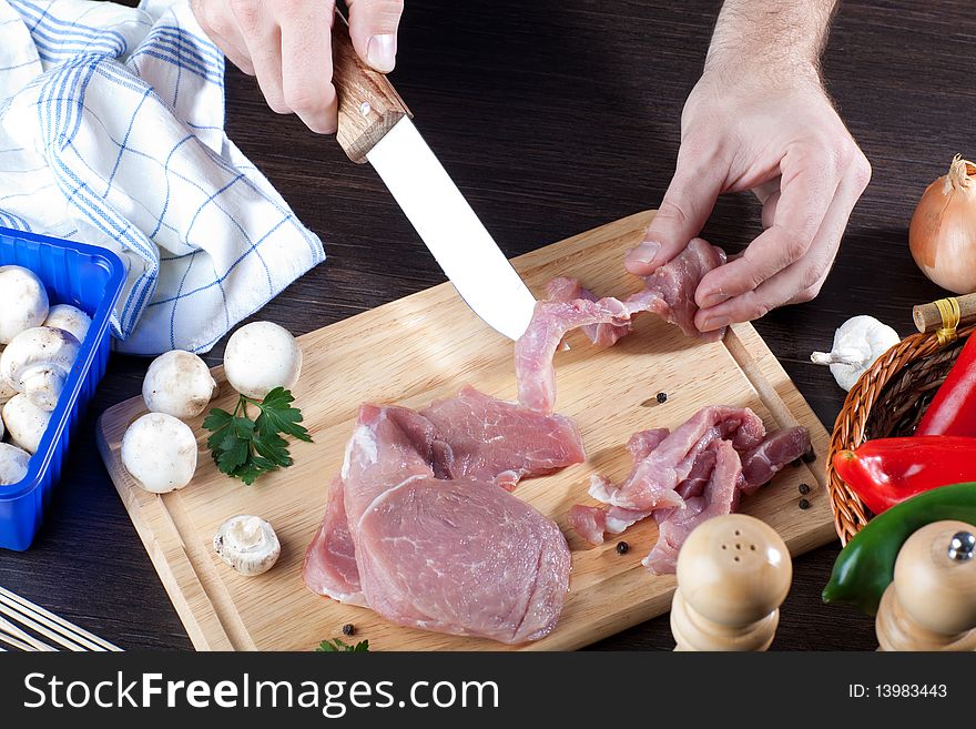 Overhead of person slicing raw pork meat on wooden board