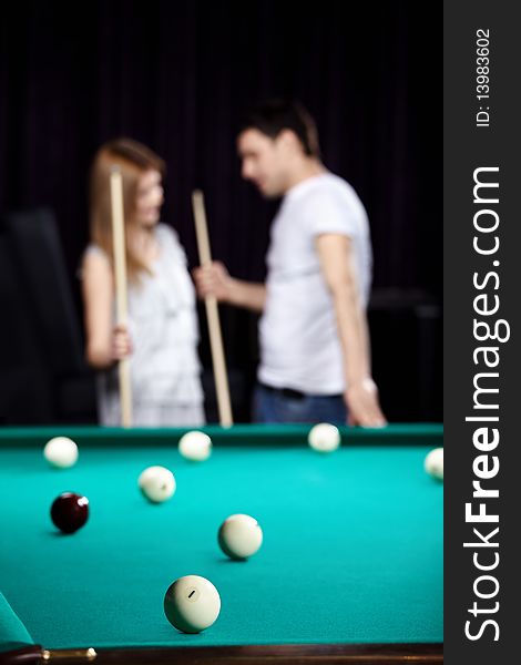 The young couple plays billiards on a back background. The young couple plays billiards on a back background
