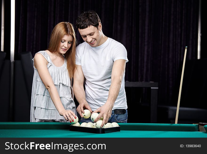 The young couple puts spheres for billiards. The young couple puts spheres for billiards