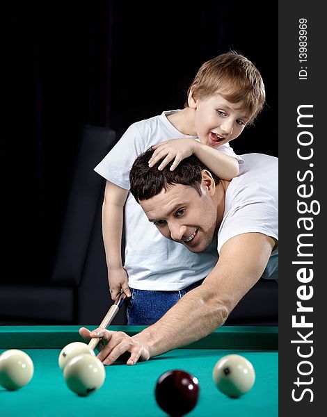 The young man and the little boy play billiards. The young man and the little boy play billiards