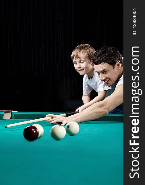 The young man and the little boy play billiards. The young man and the little boy play billiards