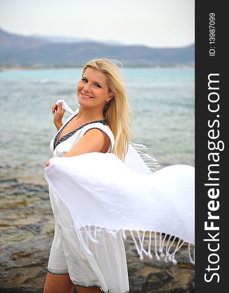 Young beautiful romantic woman in white dress dancing with shawl near blue sea